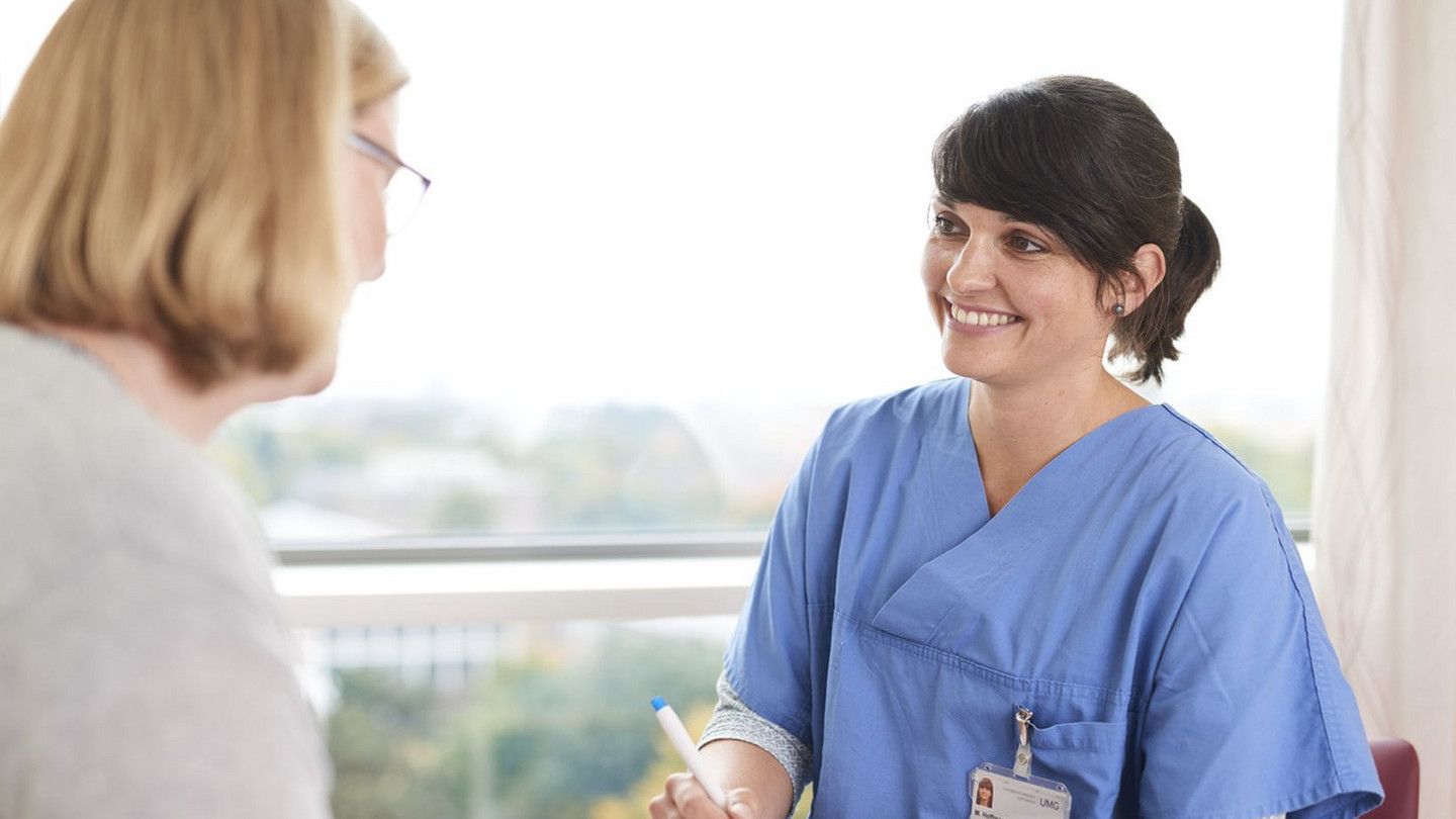 Pflegerin bei Patientin am Bett lächelnd